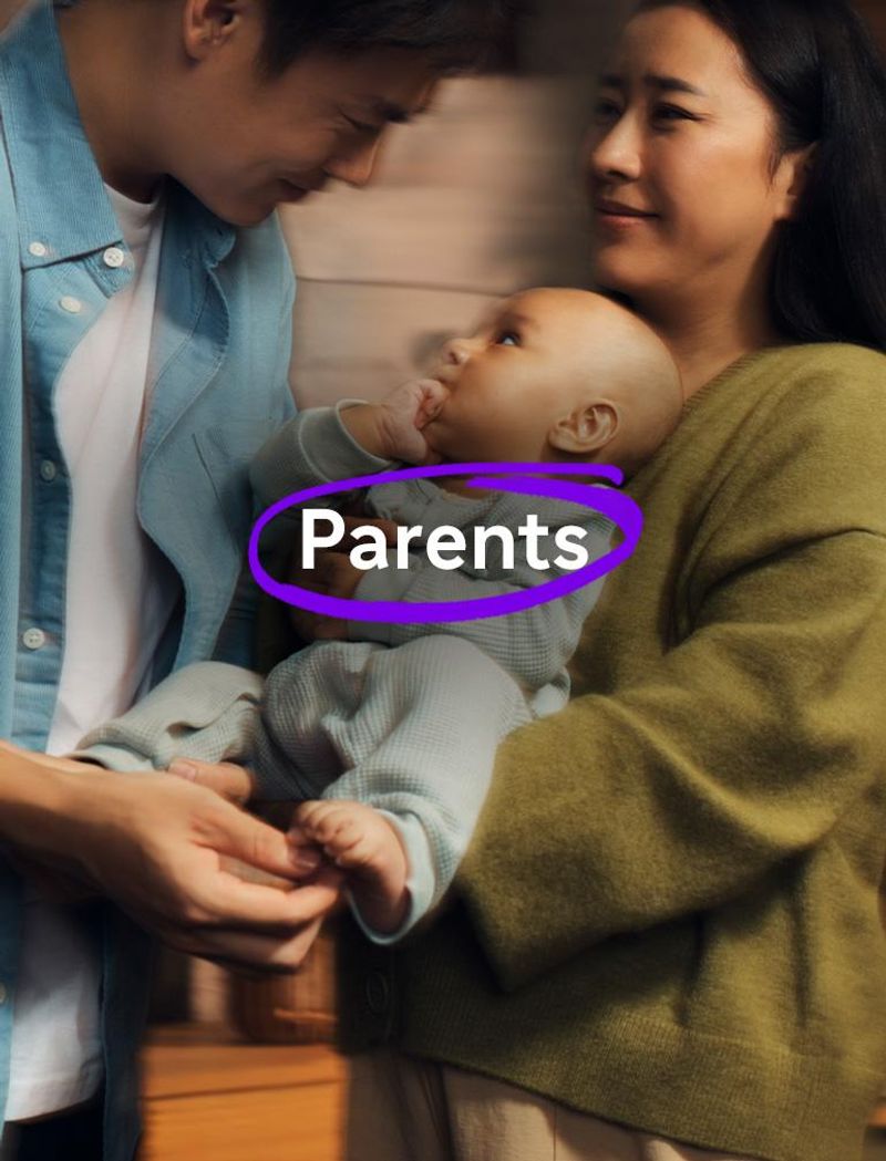 Un homme en chemise bleue et une femme en pull vert tiennent ensemble un petit bébé. Le bébé a la main dans la bouche et regarde l’homme. Le texte en surimpression indique : « Parents. » 