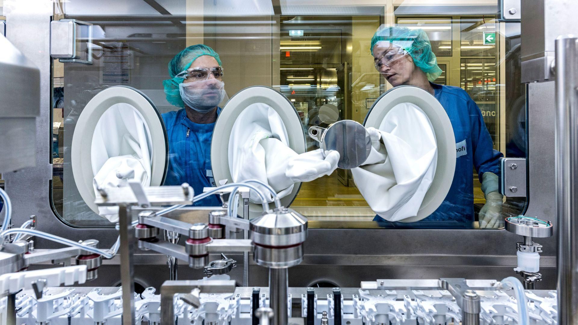 Emre Canaki and Stefanie Kutschmann pass a metal disk between them by way of gloveboxes inside a large steel machine.