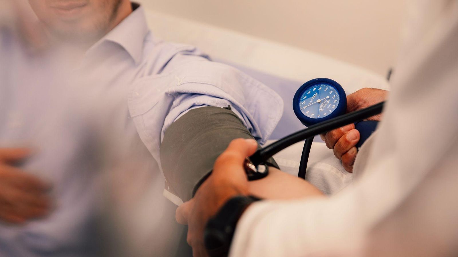 A healthcare professional measures a patient’s blood pressure using a manual cuff during a clinical check-up.