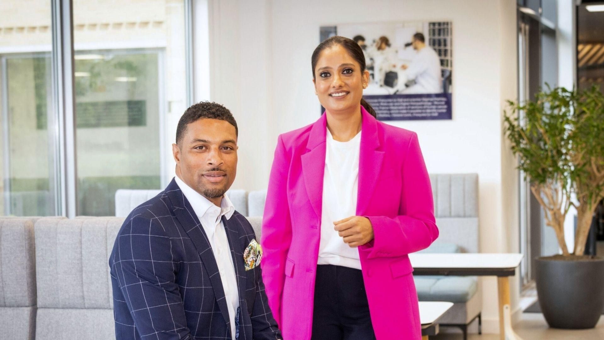 Two Sanofi professionals, a man in a dark blue checkered suit and a woman in a pink blazer, interacting in a contemporary office setting