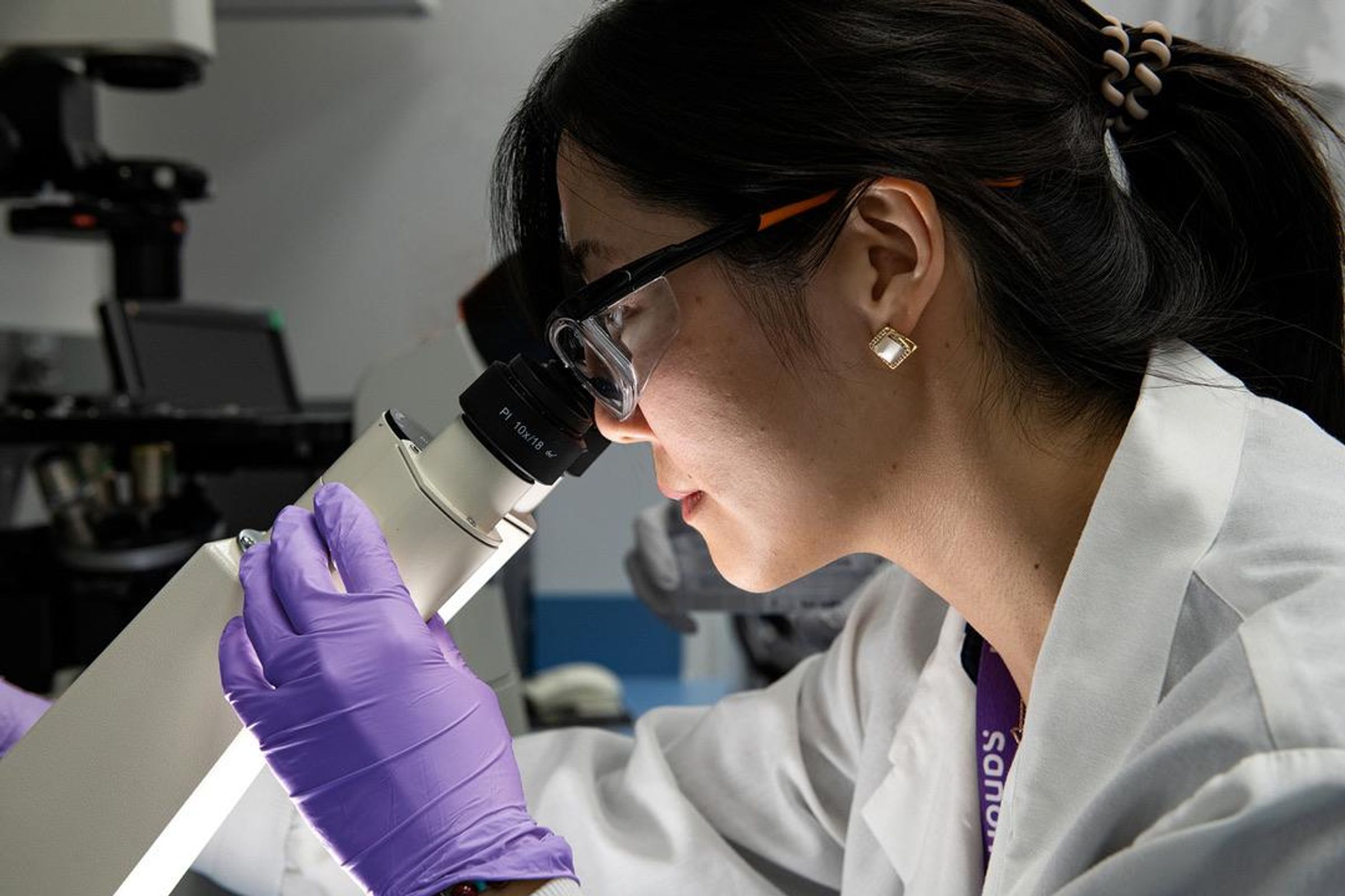 Scientist in a lab coat looks into a microscope in her lab