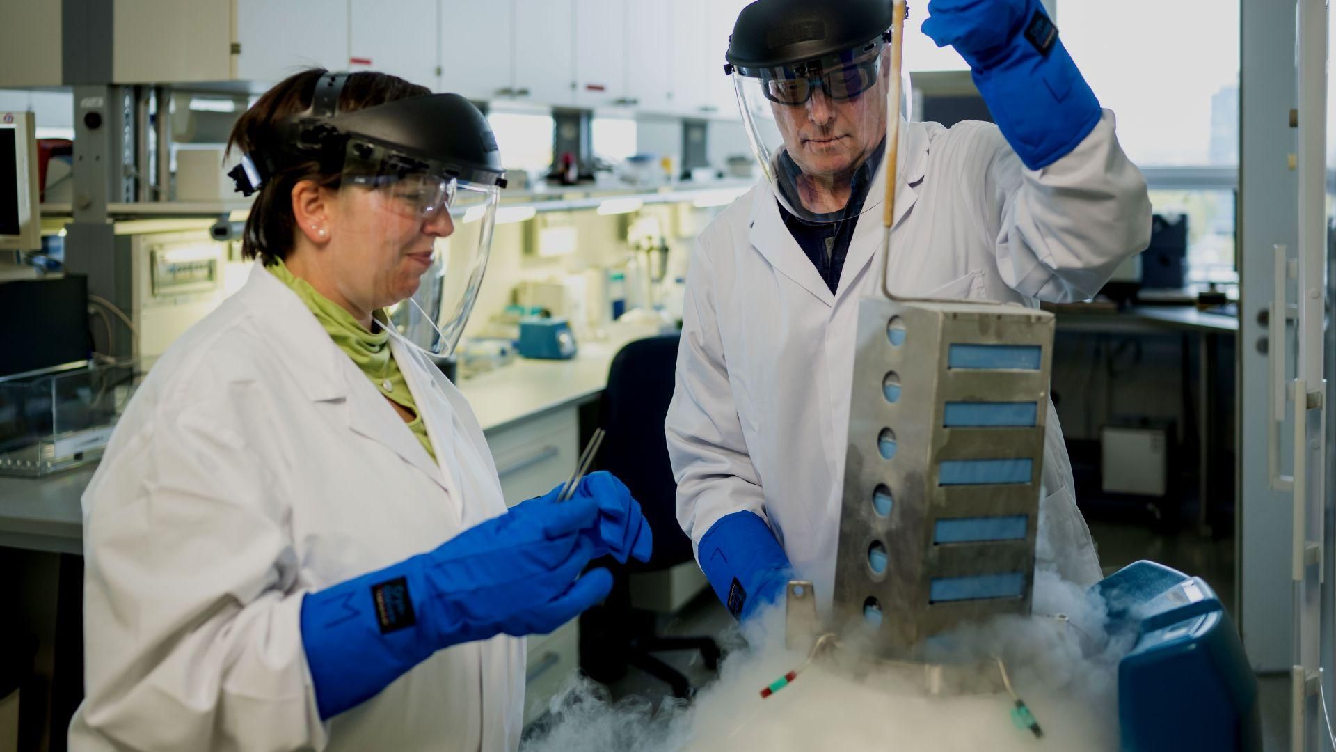 Melanie Petermann and Arno Laber wearing insulating protective gear, pull a container out liquid nitrogen in a small lab