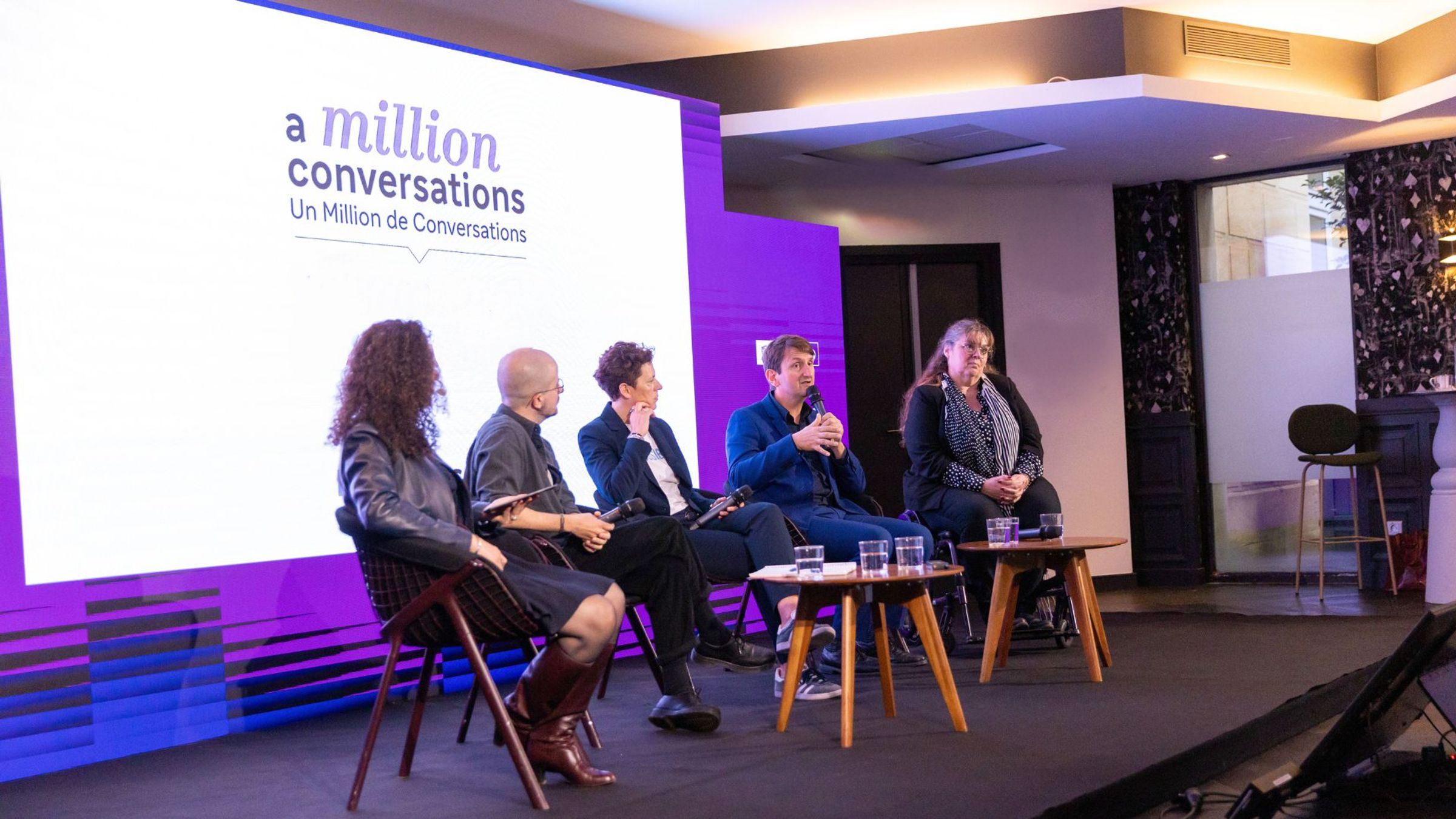 Five panellists of mixed genders seated on stage at a Sanofi event with UNESCO event in Paris. Behind them, a large screen displays the A Million Conversations logo.