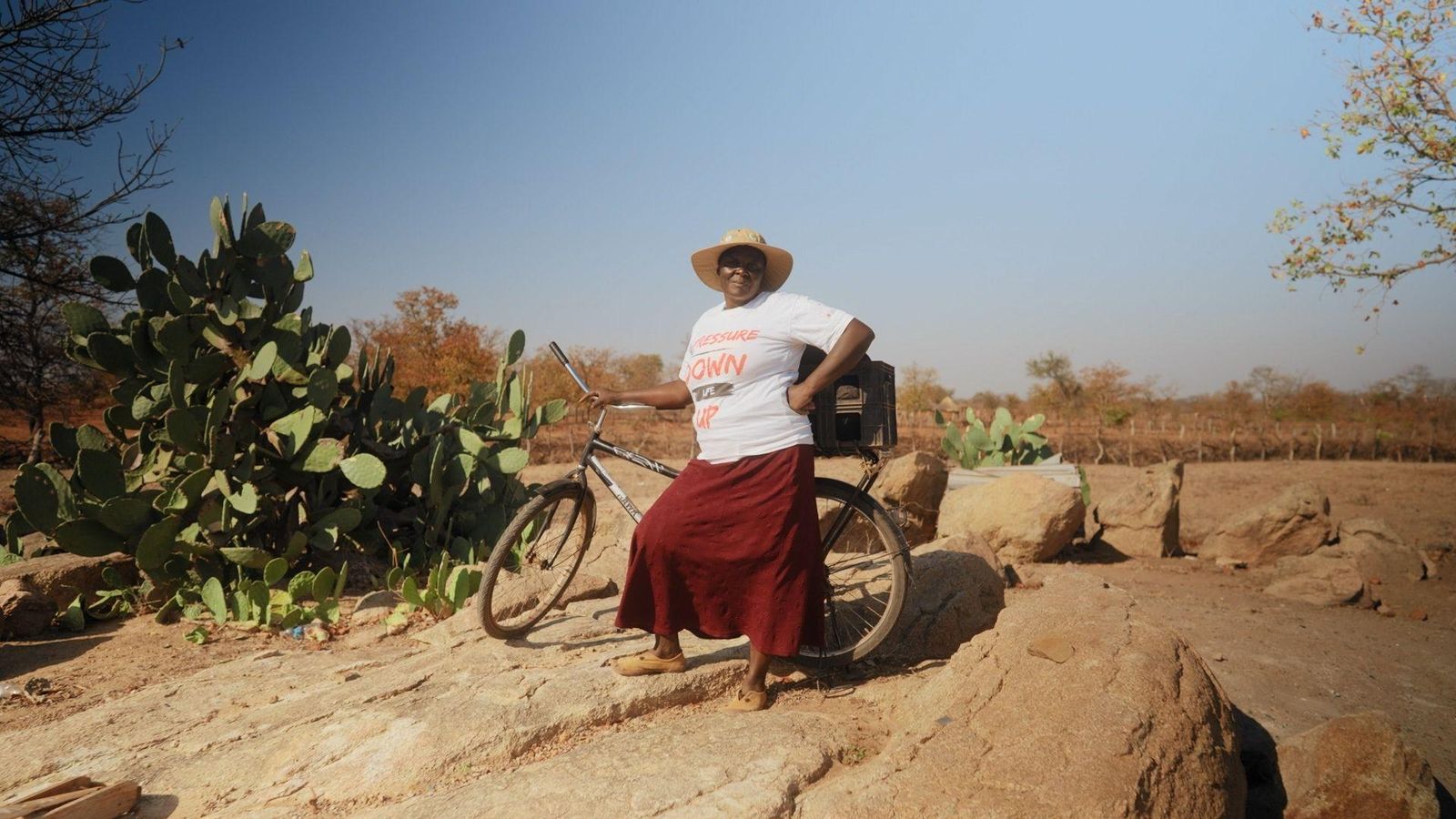 Person standing beside a bicycle outdoors in a dry, rural landscape.