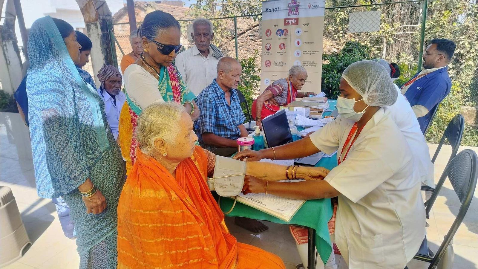Healthcare worker checks an older adult’s blood pressure at an outdoor community health event.