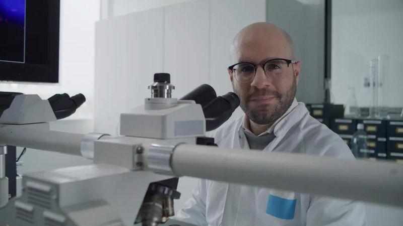 Nizar El Murr working with a microscope in a laboratory, wearing a lab coat