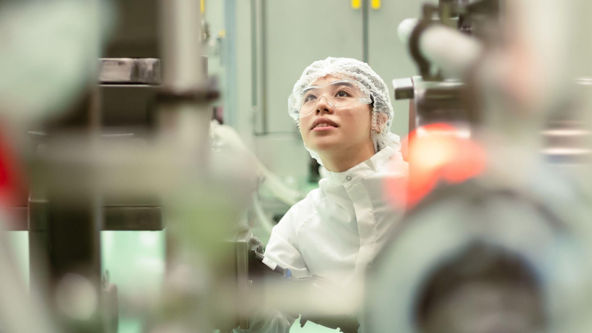 Aurora Loh, a biotechnologist in protective gear, inspecting large-scale machinery at Sanofi Modulus Singapore. 